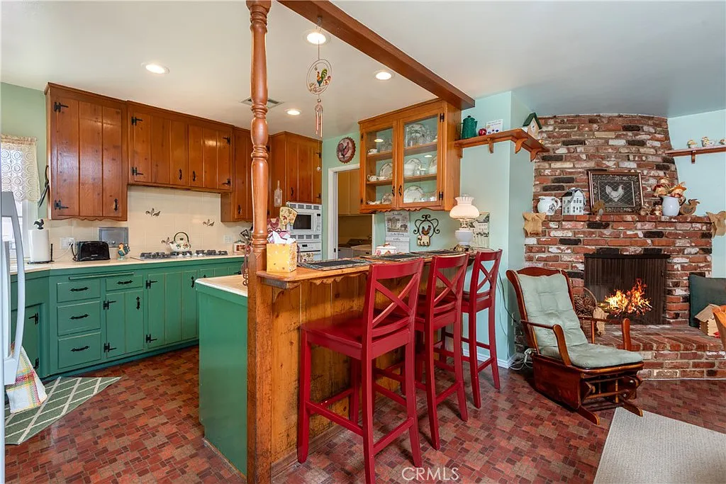 kitchen with wooden cabinets, green island, bar stools, and brick fireplace