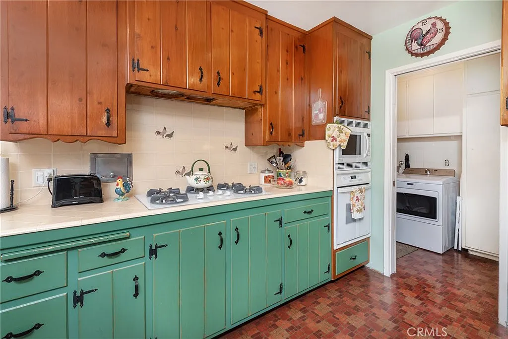 Kitchen with warm wooden cabinets, green lower section, gas stove, oven, and wall decorations