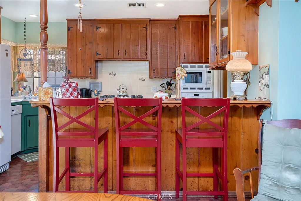 Kitchen with wooden cabinets, bar counter with red stools, and appliances