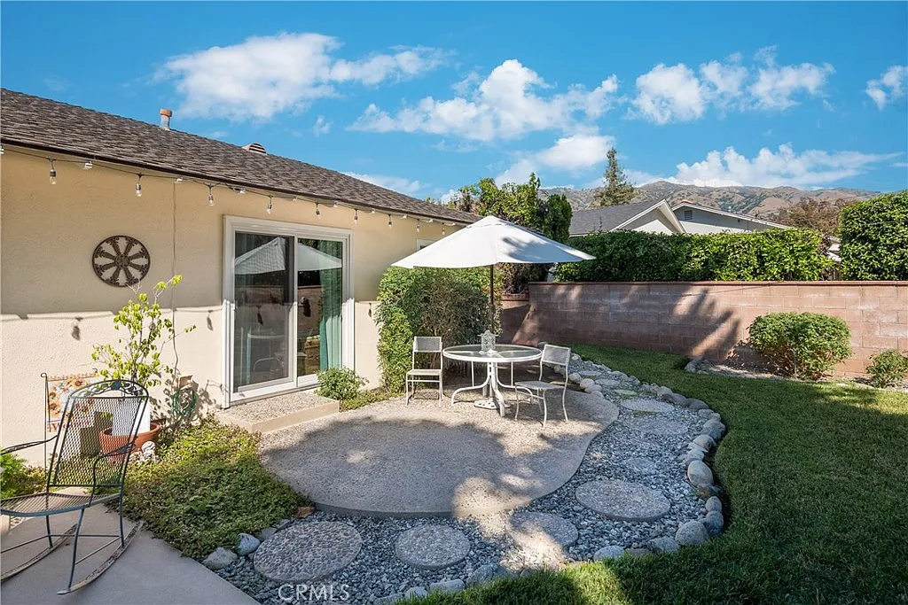 Backyard with round table, chairs under umbrella, gravel, and landscaped greenery