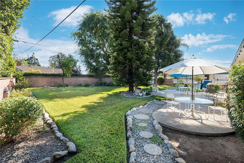 Backyard with grassy area, tall tree, and patio set with umbrella