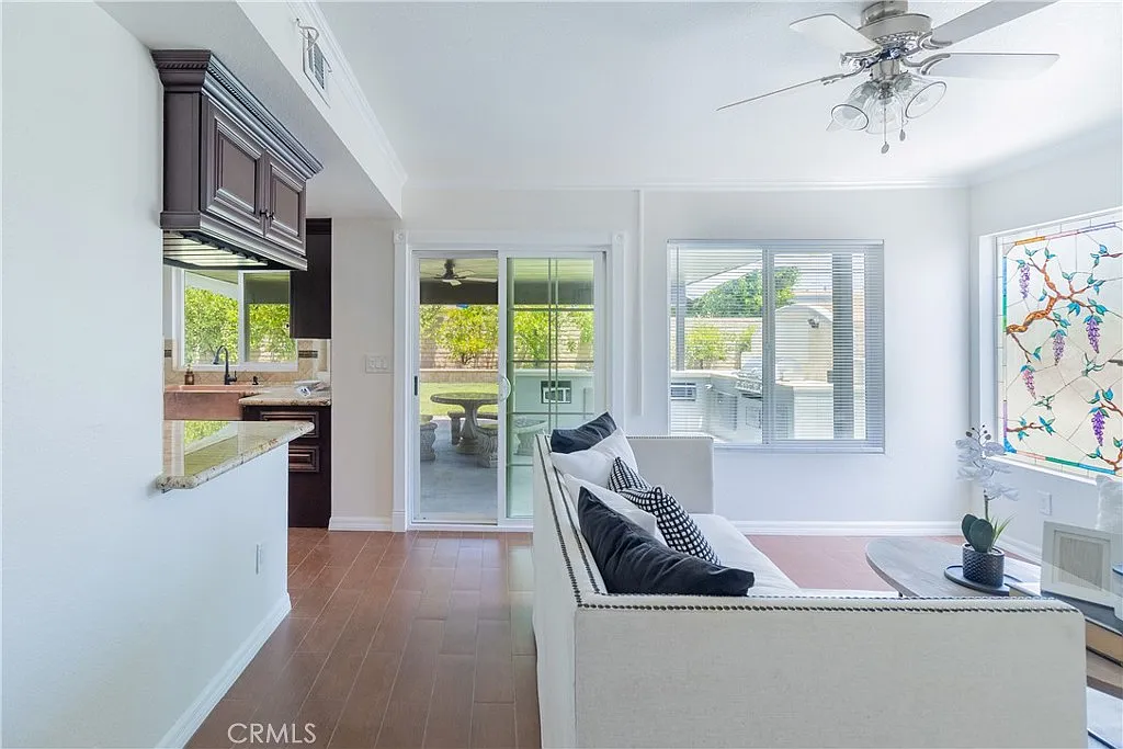 living room with white sofa and black-and-white pillows, kitchen with dark cabinets, large windows, and sliding door to outdoor greenery.
