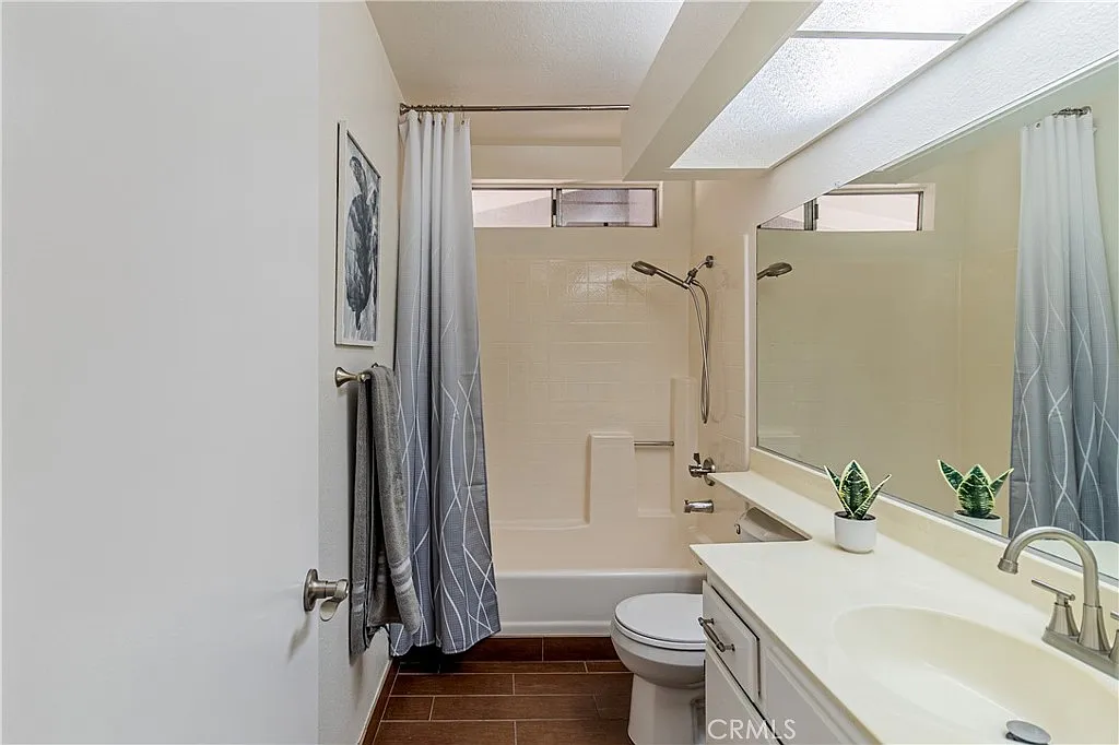 Modern bathroom with tub and shower, large mirror above sink, neutral walls, and decorative plants.