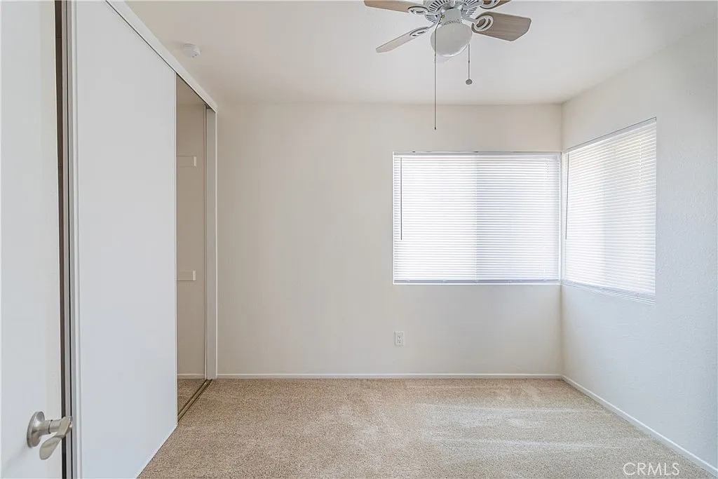 Room with beige carpet, ceiling fan, white walls, window with blinds, and partially visible closet door.