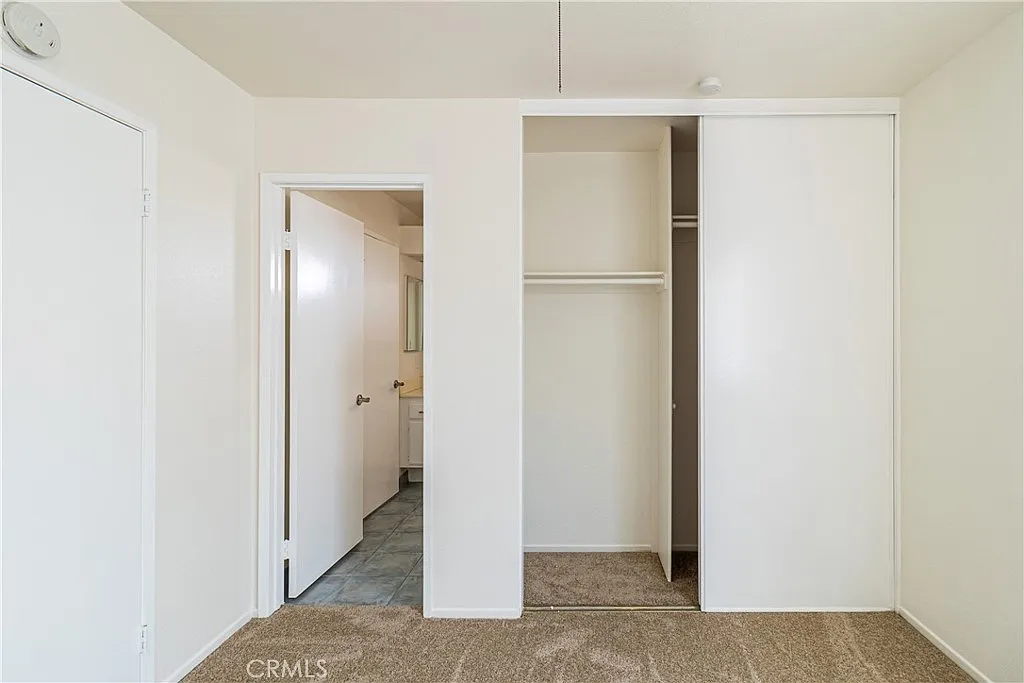 Vacant room with white closet with sliding doors, closed door to another room, light-colored walls, and beige carpet.