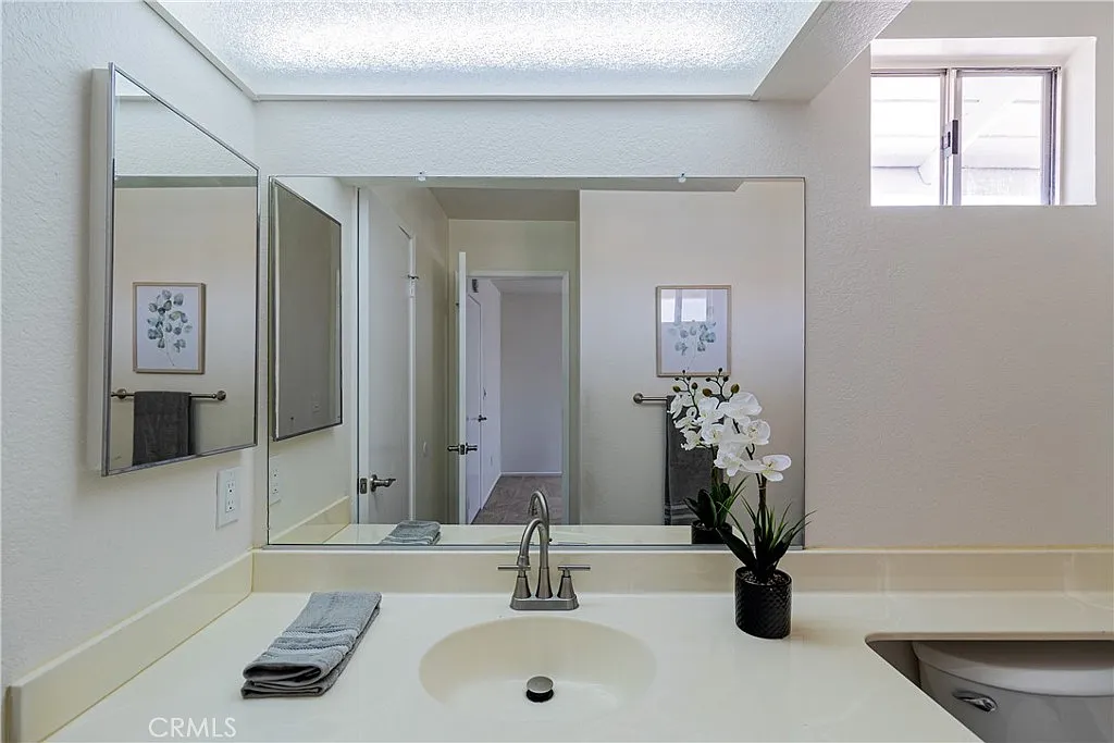 bathroom with mirror above sink, small potted plant, neatly arranged towels, and doorway to another room.