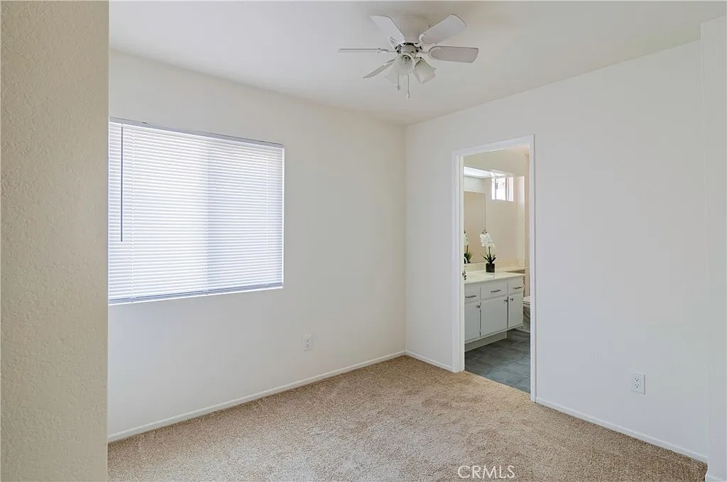 Light-colored room with window, carpeted floor, ceiling fan, and doorway to area with bathroom.