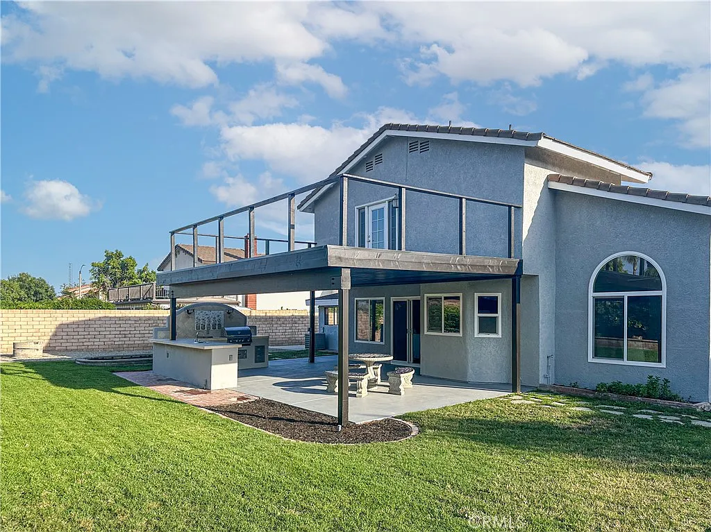 Two-story house with balcony, patio with outdoor kitchen, and well-maintained lawn, real estate.