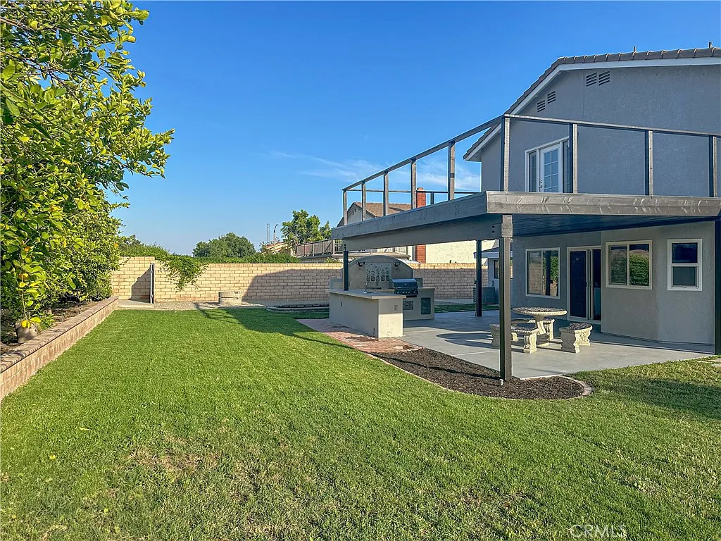 Backyard view of house with patio, grass lawn, and barbecue area, real estate.