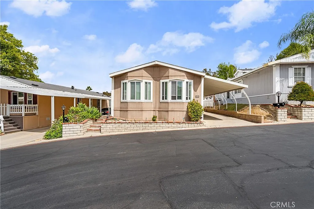 Beige manufactured home California real estate with windows, driveway, road, and greenery.