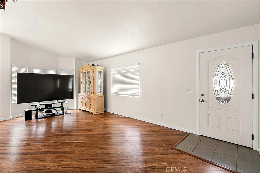 Living room with flat-screen tv, wooden cabinet, front door with decorative glass, hardwood floor and white walls