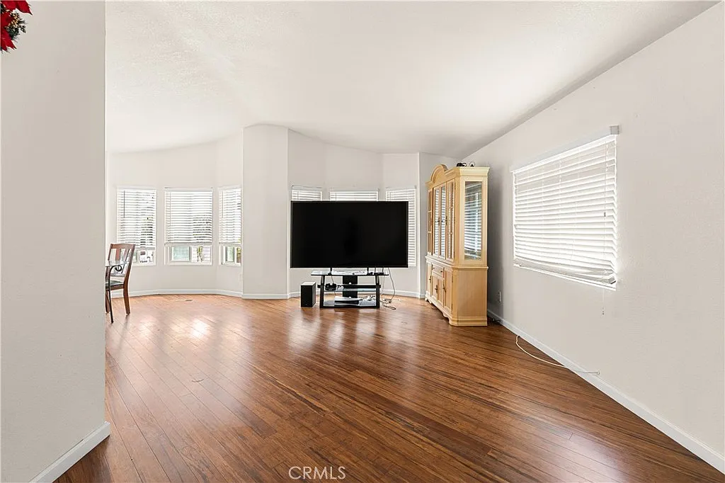 Living room with wooden floor, large windows with blinds, flat-screen tv, and entertainment unit.