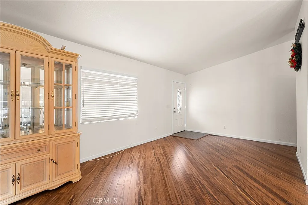 Empty living room with glass-front cabinet, door with window, and light-colored walls.