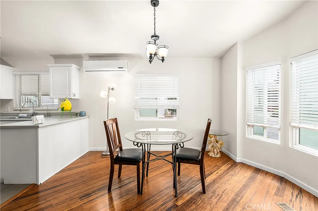 Kitchen and dining area with round glass table, two wooden chairs, hardwood floor, and natural light from windows.