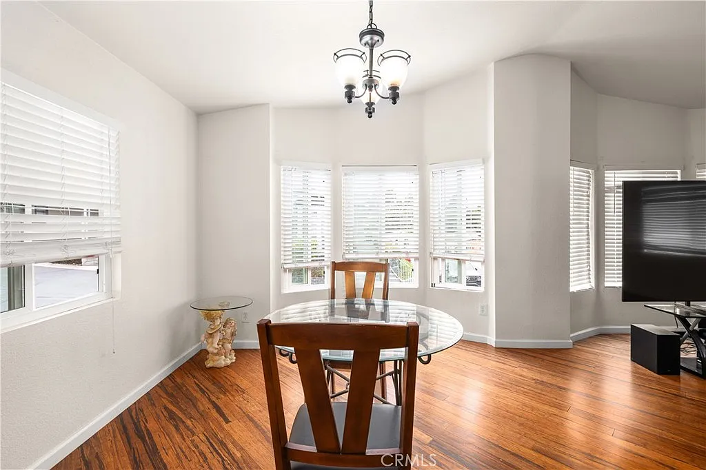 Right dining area with round glass table, wooden chairs, large windows with white blinds, and hardwood floor.
