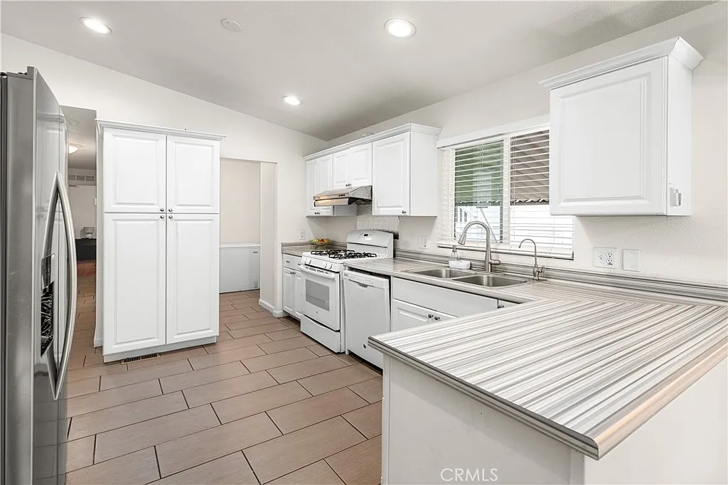 Kitchen with white cabinets, stainless steel appliances, tiled floor, gas stove, double sink, and ample counter space.