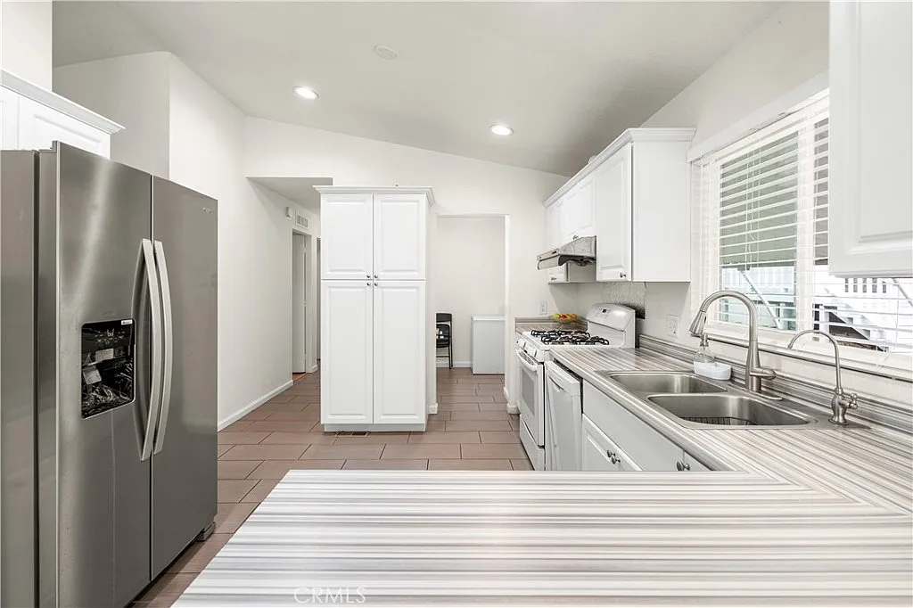 Kitchen with white cabinets, stainless steel appliances, striped countertop, and natural light from windows.