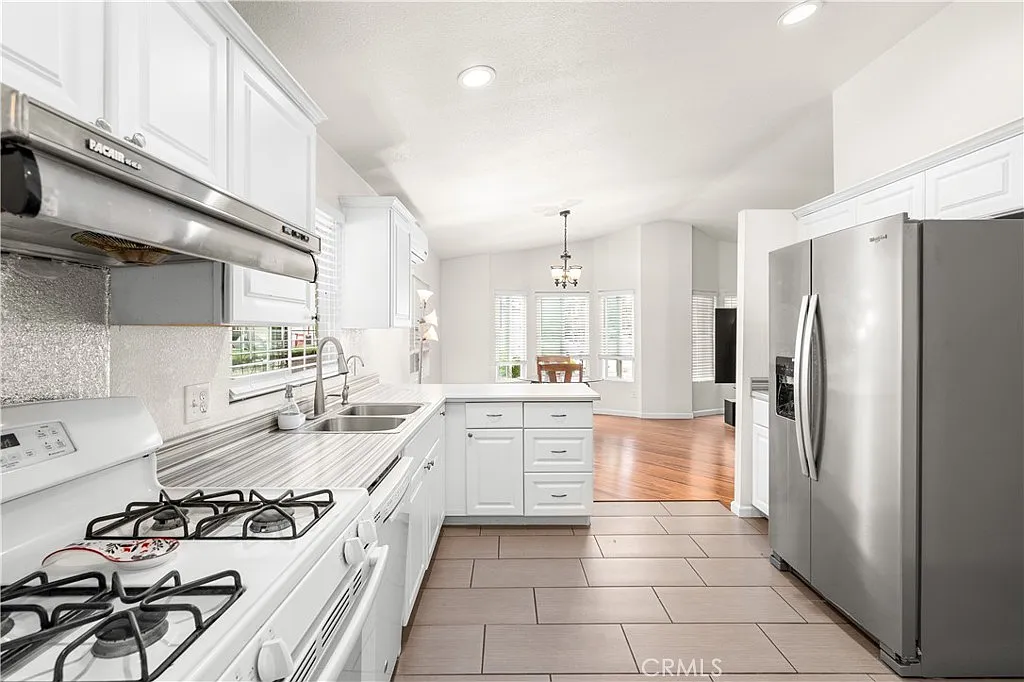 Kitchen with white cabinets, stainless steel appliances, gas stove, tile floor, windows, and open view to dining area.