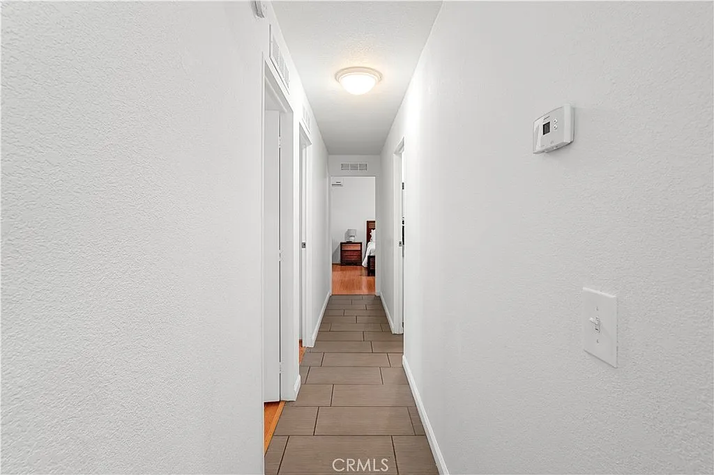 Hallway with white walls, tiled floor, light fixture, and multiple doorways.