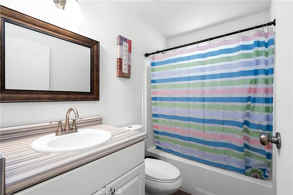 Bathroom with sink and mirror, bathtub with striped shower curtain, and toilet.