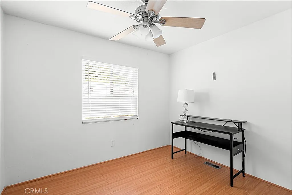 Room with ceiling fan, window blinds, and small desk.