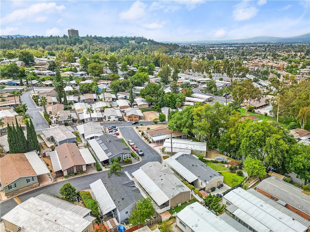 Aerial view of residential area with mobile homes, trees, and hills in the background, California real estate.