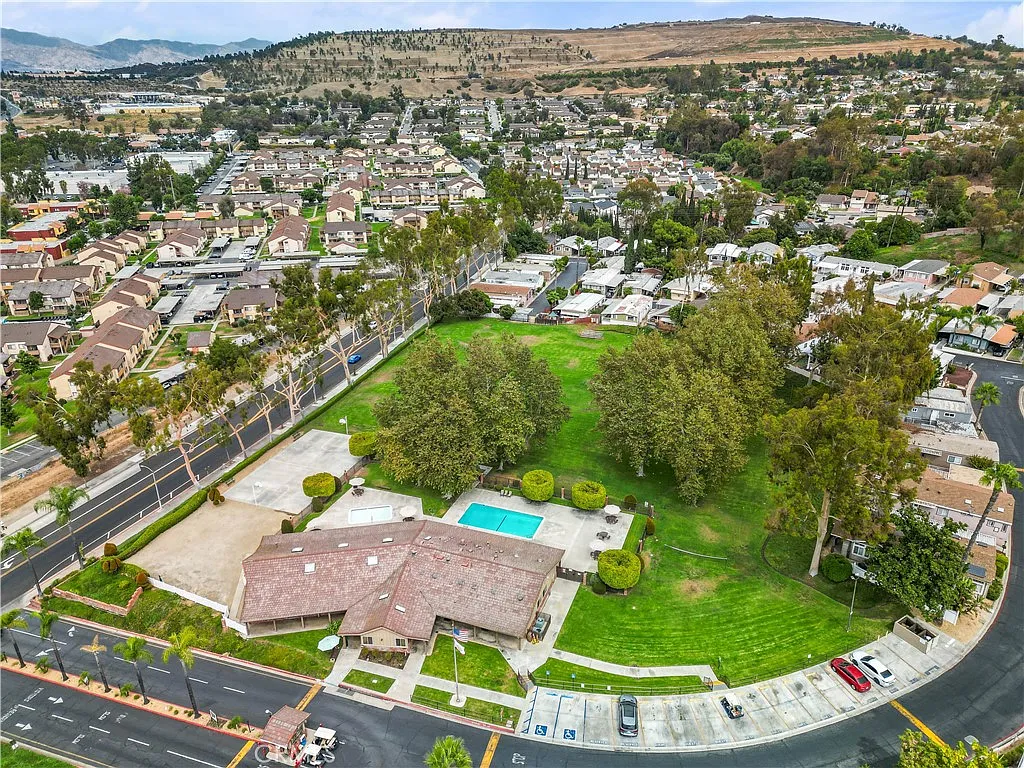 Aerial view of suburban area with homes, roads, green park with trees, and swimming pool, California real estate.