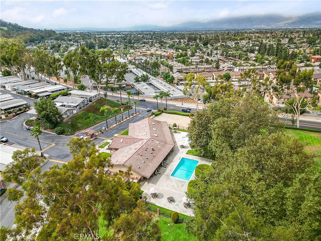 Aerial view of single-story house California real estate with pool, trees, roads, and nearby buildings.