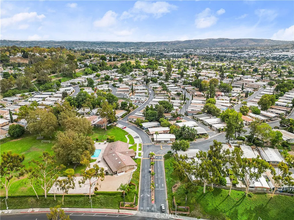 Aerial view of suburban neighborhood with winding roads, green spaces, houses, trees, and hills in the background, California real estate.