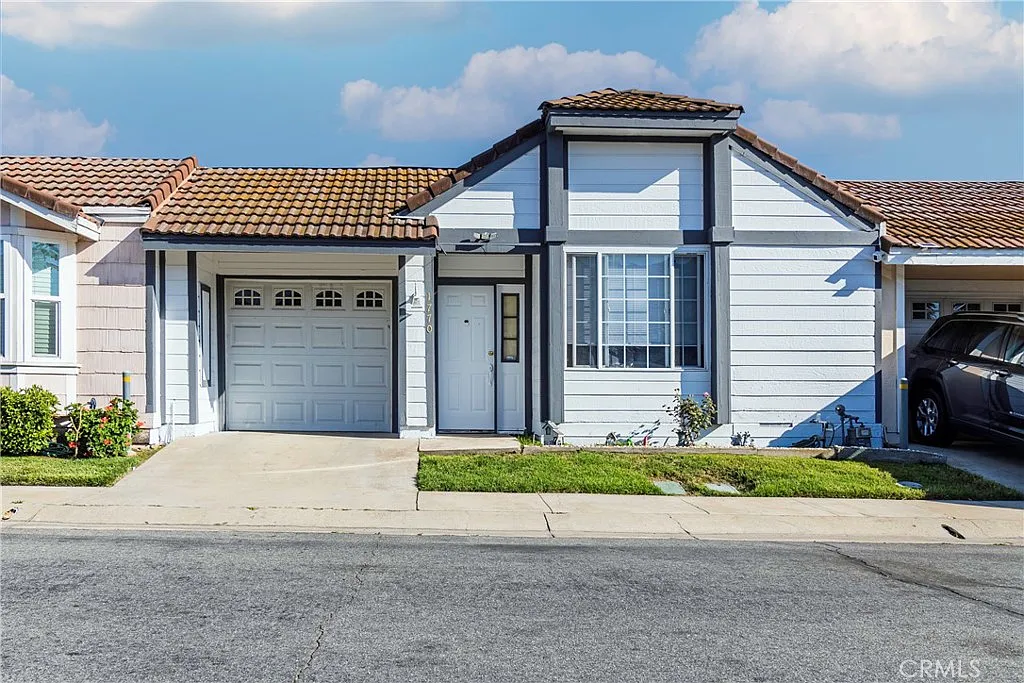 Single-story house with light blue siding, brown roof, small front yard, and garage door on the left, real estate.