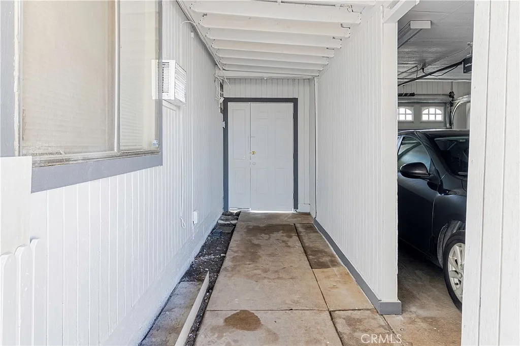 Narrow hallway with light gray wall, concrete floor, leading to closed door.