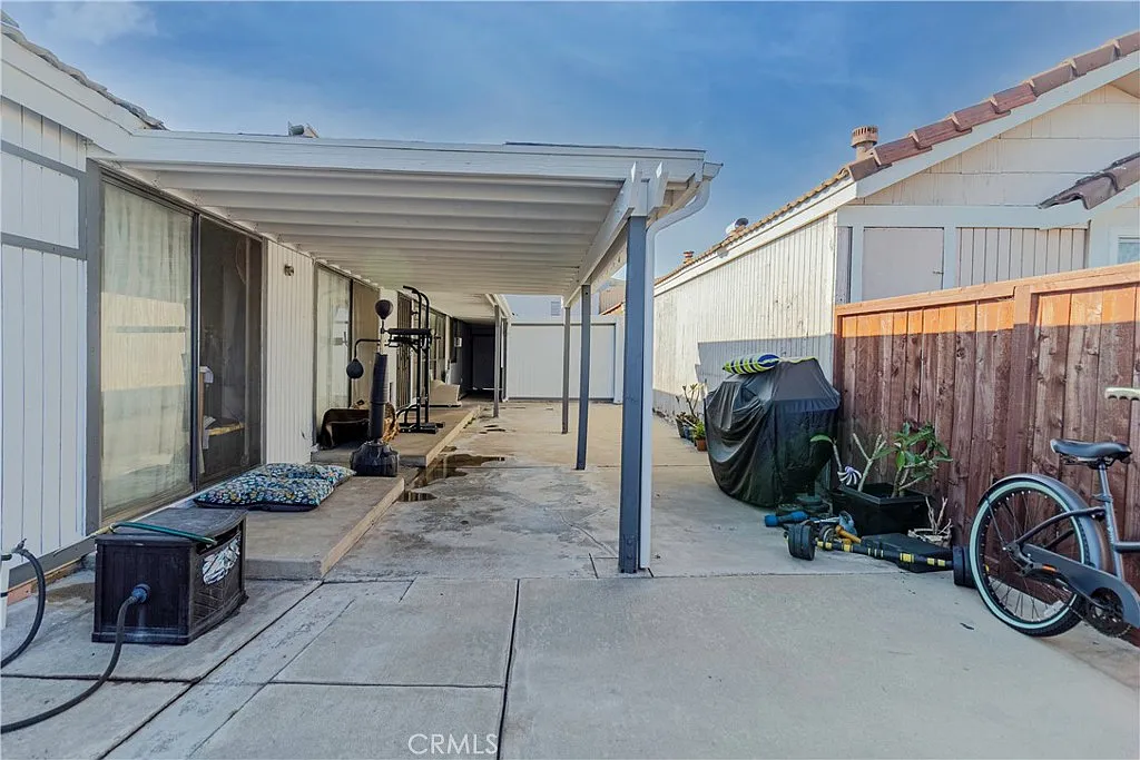 Patio with covered area, exercise equipment, potted plants, bicycle, and water pooling on the ground.