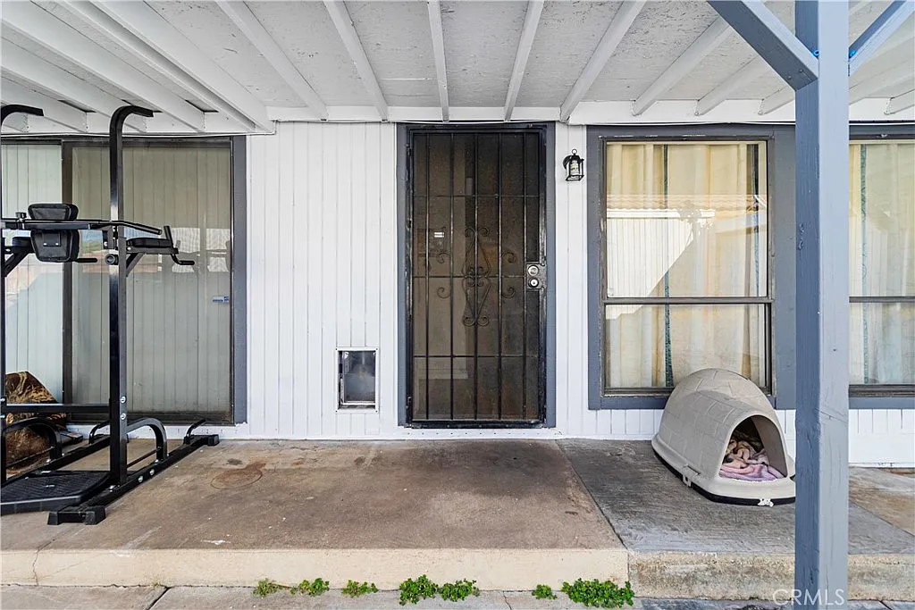 Front porch with door, windows, small dog house, and outdoor equipment.