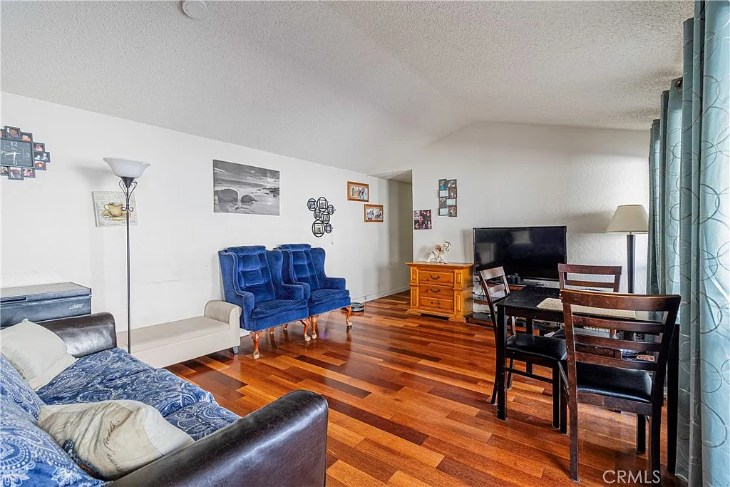 Living room with blue armchairs, dark leather couch with blue throw, hardwood floor, TV on stand, and wall decorations.