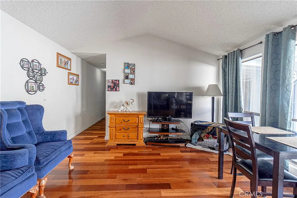 Living room with blue chairs, wooden TV stand, TV, framed pictures, window with sheer curtains, and wooden floor.
