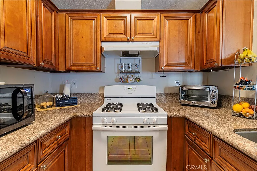 Kitchen with wooden cabinets, countertop with appliances, and white gas stove with exhaust hood.