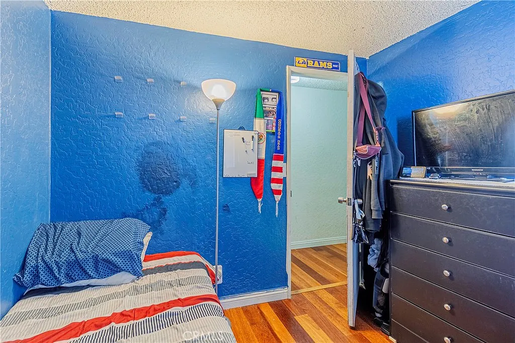 Bedroom with blue walls, bed with striped bedding, floor lamp, closed door, and TV on dresser.