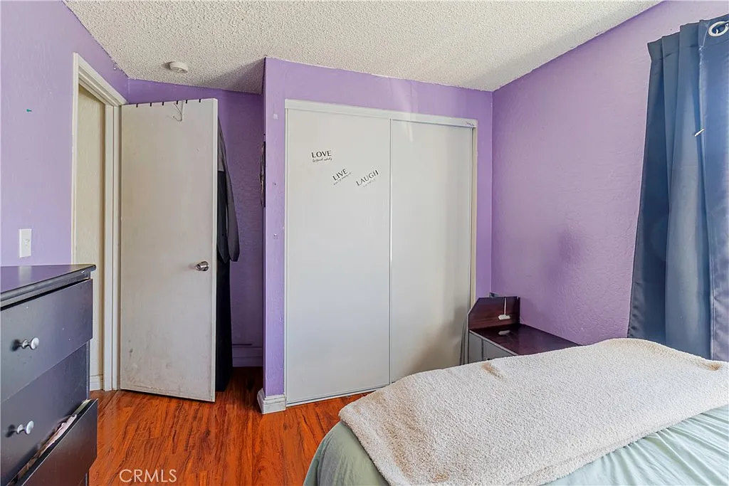 Bedroom with purple walls, closet with white sliding doors labeled "LOVE," bed with light blanket, dresser, and doorway to another room.