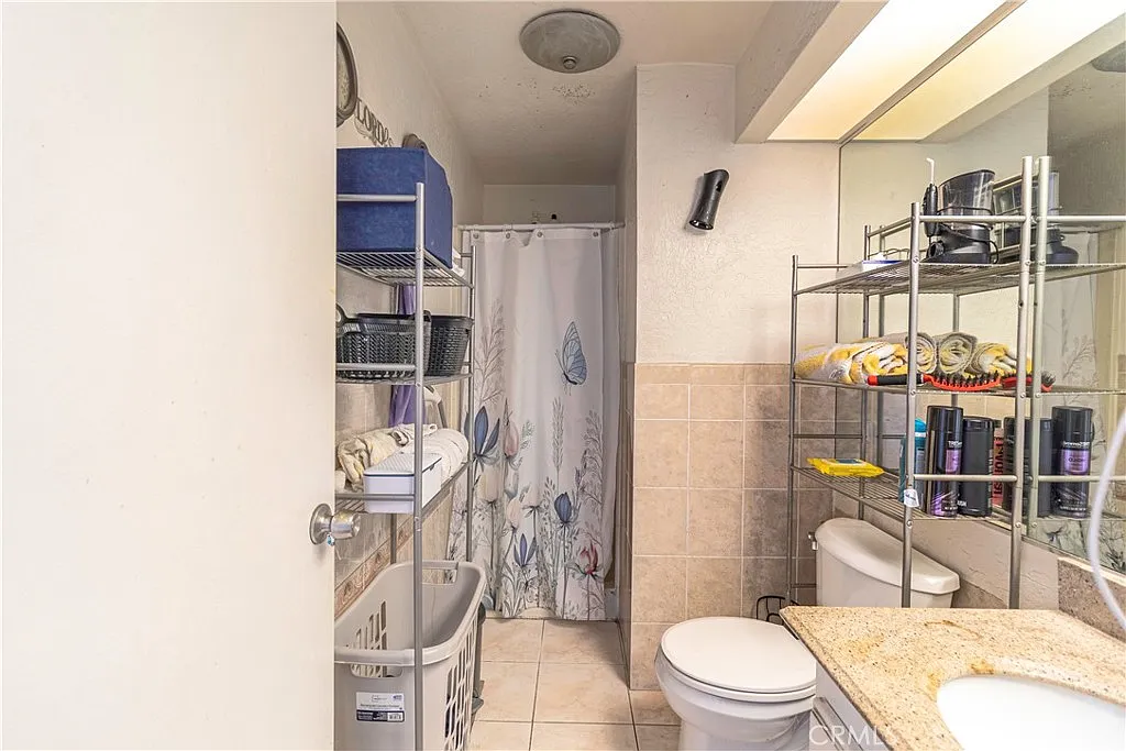 Bathroom with shower curtain, shelves with toiletries and towels, laundry basket, and toilet.
