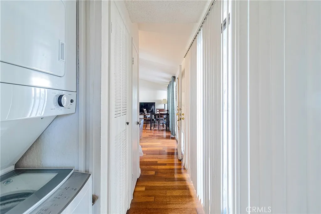Hallway with white walls, hardwood floor, laundry machine on the left, leading to living area.