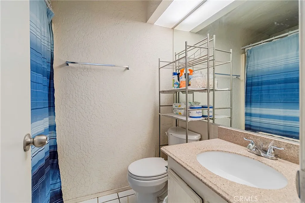 Bathroom with toilet, sink and countertop, shelving with toiletries, and blue striped shower curtain.