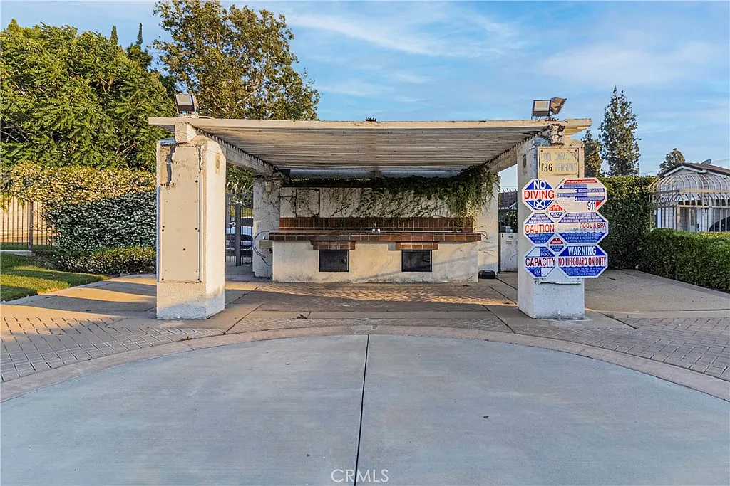 Covered outdoor structure with wooden bench, greenery, and nearby signs.