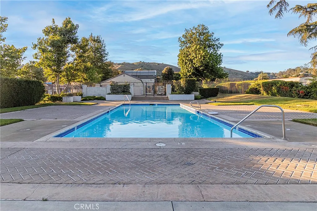 Clear swimming pool in landscaped area with trees and hills in the background.