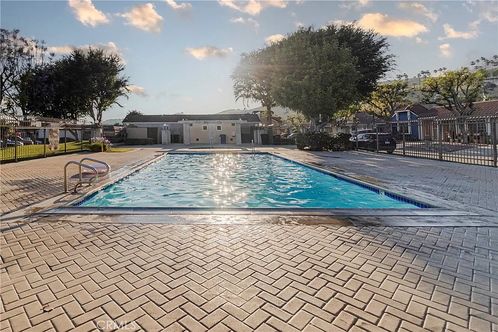 Swimming pool with paved plaza, trees, and buildings in the background.