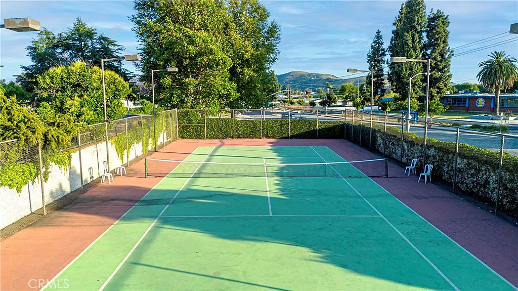 Tennis court with green and red surfaces, trees and fence around, in sunny outdoor setting.