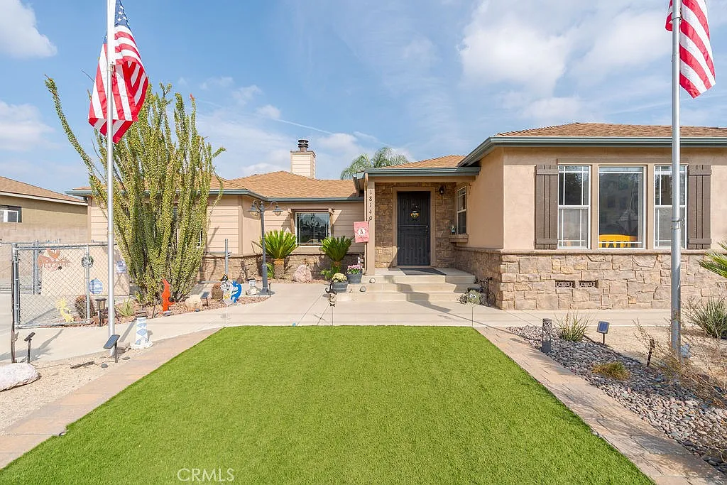 A front view of a house with a manicured lawn, two American flags, and desert landscaping.