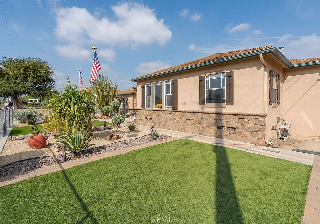 A single-story home with a stone facade, landscaped front yard with grass, plants, decorative stones, and flags.
