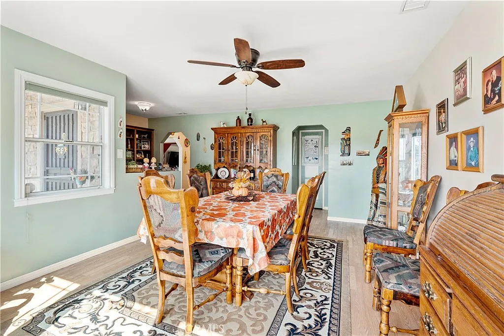 Dining room with a large wooden table, chairs, ceiling fan, decorative furniture, light-colored walls, and a patterned rug.