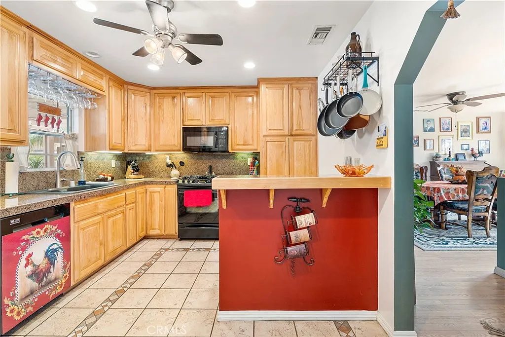 Kitchen with wooden cabinets, granite countertop, dark oven and stove, red wall with hanging pots, a shelf with cookbooks, and a dining area visible through an arch.