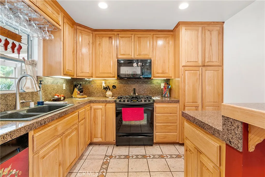 A kitchen with wooden cabinets, granite counters, a black stove, and tile floors.